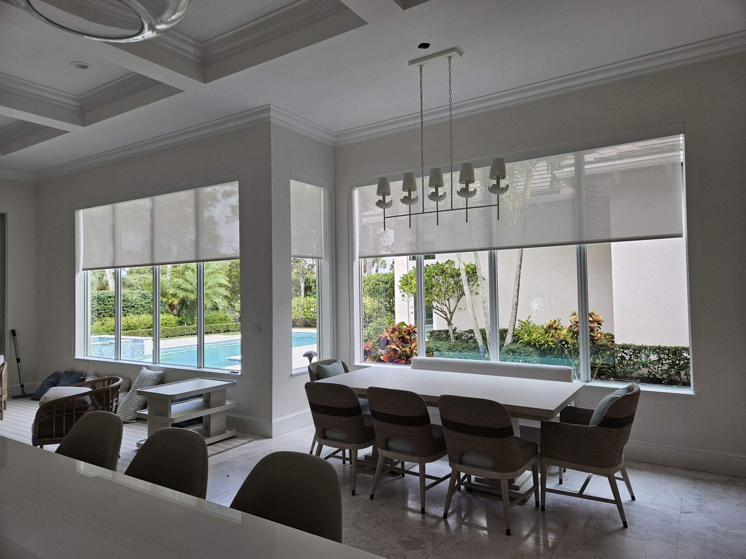 Motorized solar shades reducing glare while preserving pool and garden views in a Palm Beach County home
